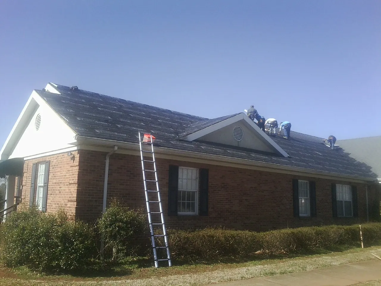 Crew tearing shingles off a brick ranch roof with a ladder set — Metal Roof Repair work by our crew in French Lick