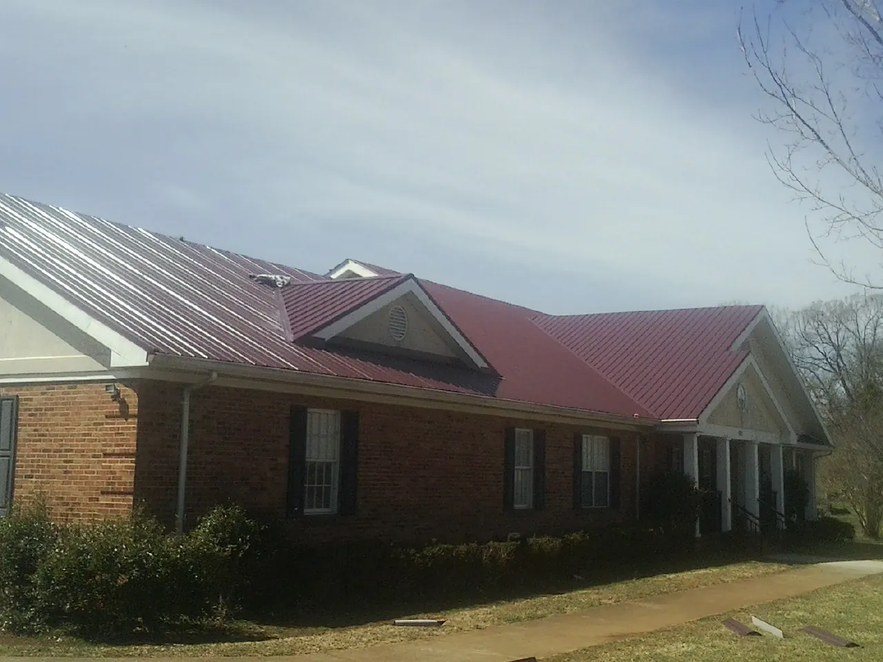 Red metal roof with gabled entries on a long brick building, from a Hail Damage Roof Repair job in French Lick