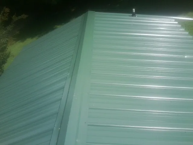 New green metal panels meeting at the ridge of a roof — Flat Roof Repair work by our crew in French Lick
