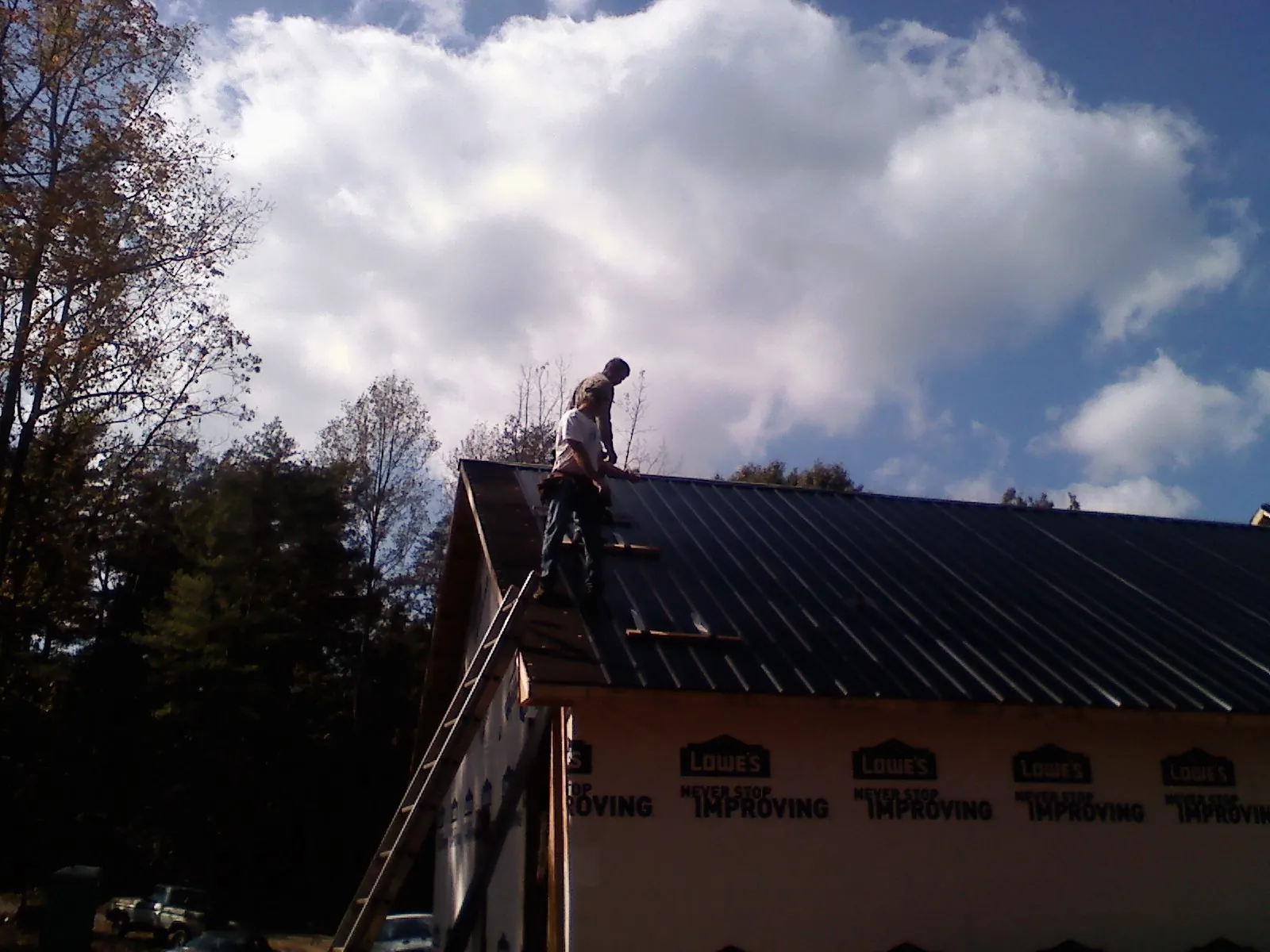 Roofer fastening dark metal panels high against a cloudy sky, from a Roof Inspection job in French Lick