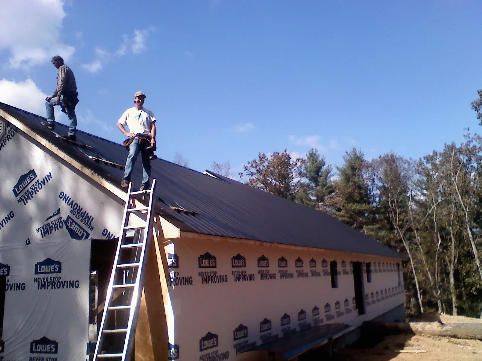 Two roofers standing on a long dark metal roof over a wrapped building in French Lick