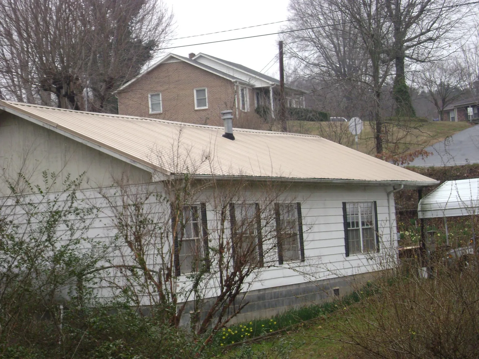 Tan metal roof on a white sided house set into a hillside — Commercial Roofing by Roofing Brothers in French Lick